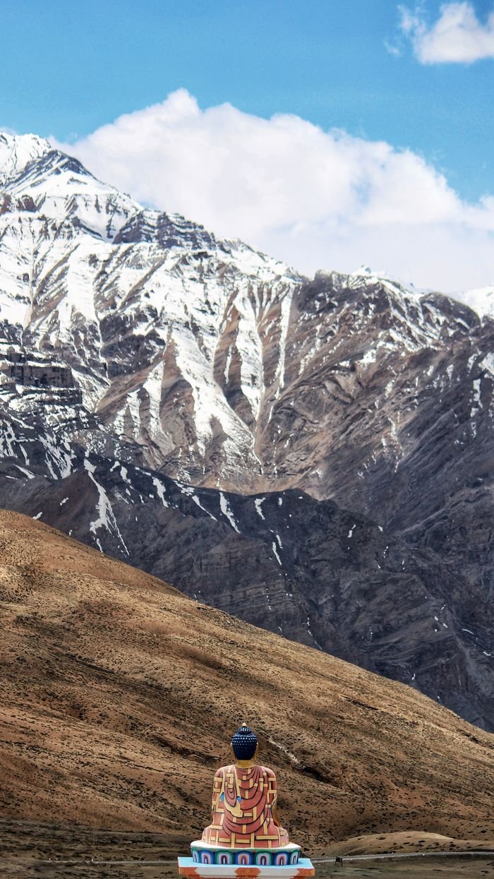 Buddha statue overlooks breathtaking snow-capped Himalayas, a serene travel destination.